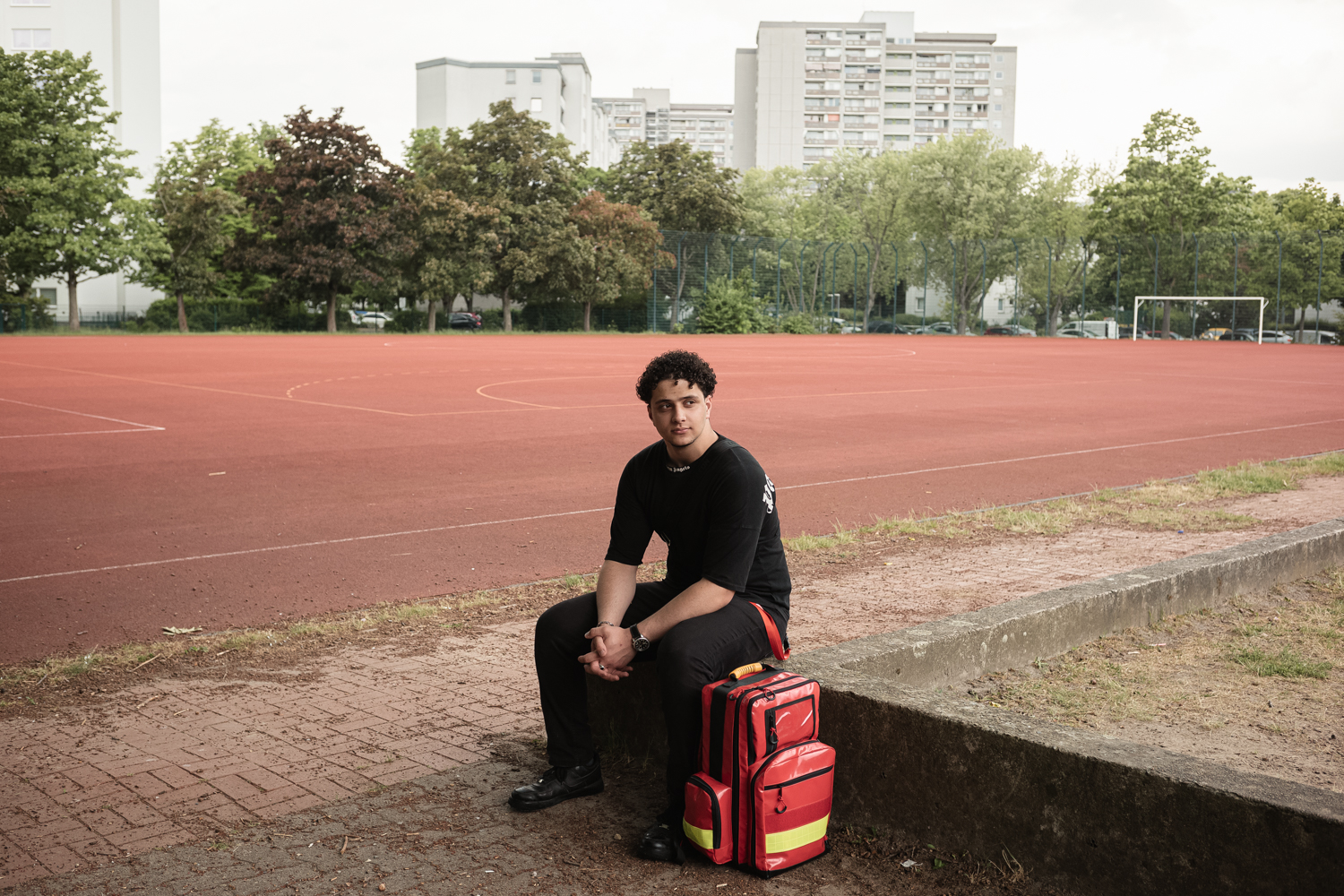 Talent Homam sitzt auf einer Steinmauer und neben ihm steht sein Erste-Hilfe-Rucksack